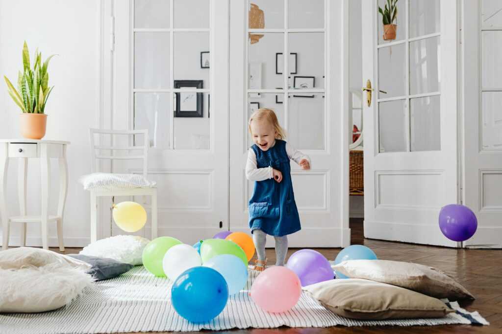 A cheerful young girl enjoying a playful moment with colorful balloons in a bright indoor setting.